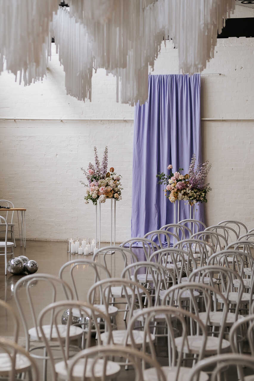 Altar de casamento decorado com cortina lilás e arranjos florais em tons suaves