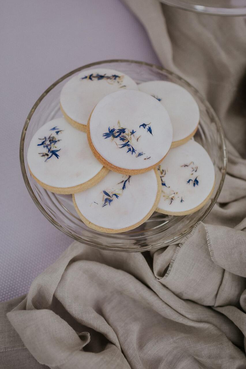 Cookies decorados com flores roxas e brancas sobre um prato de vidro.