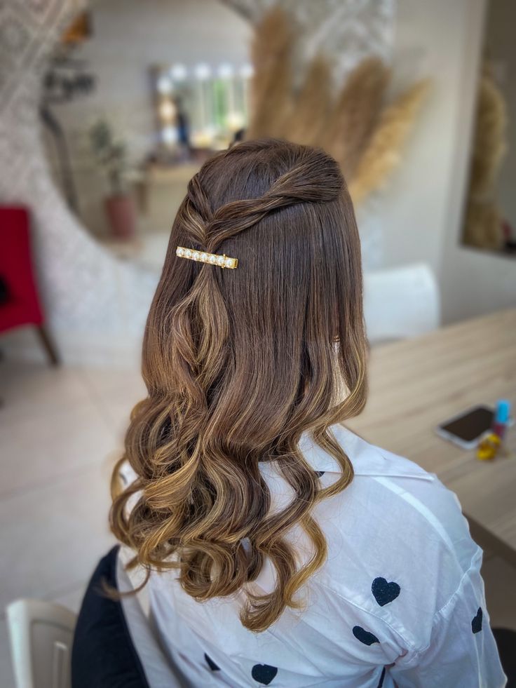 Mulher com cabelo castanho preso parcialmente, usando uma delicada presilha dourada enquanto mantém as ondas soltas no cabelo.