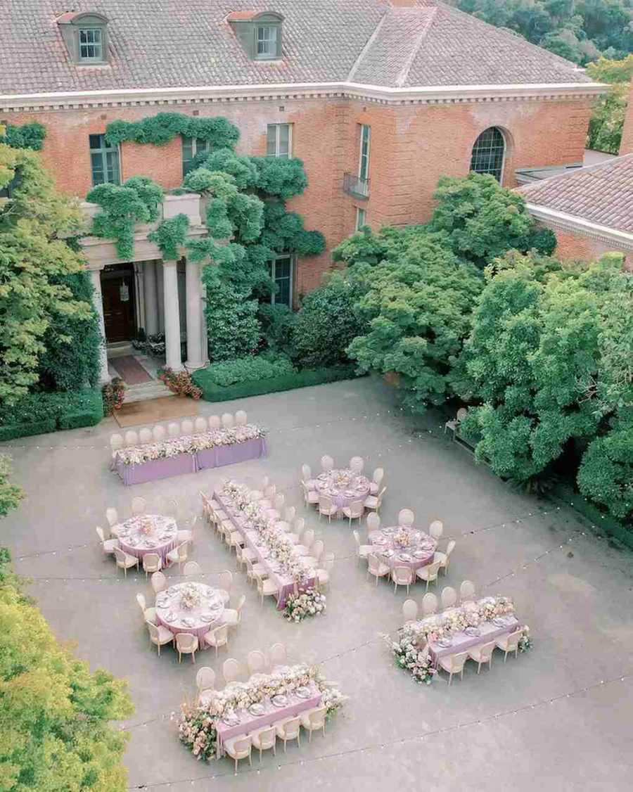 Vista aérea de um casamento ao ar livre com mesas decoradas com toalhas lilás e arranjos florais