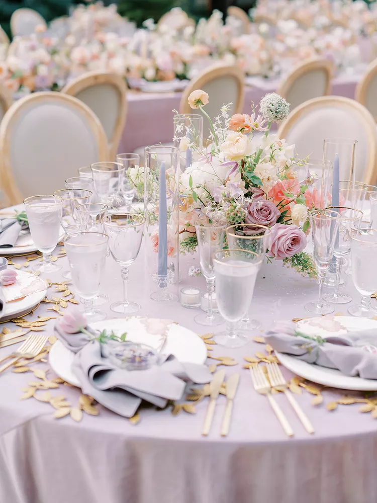 Mesa de casamento ao ar livre com toalha lilás, arranjo floral vibrante e cadeiras elegantes