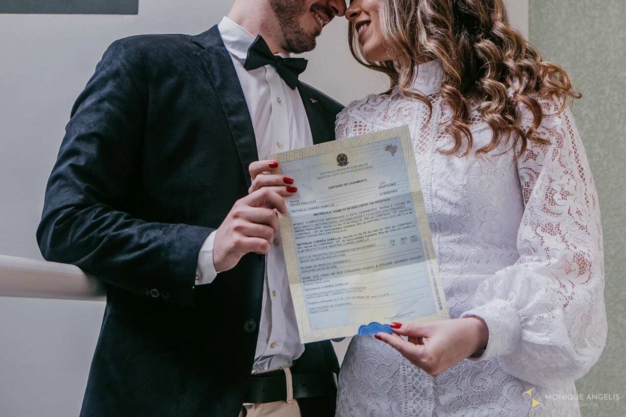 Casal recém-casado sorrindo enquanto segura a certidão de casamento oficial