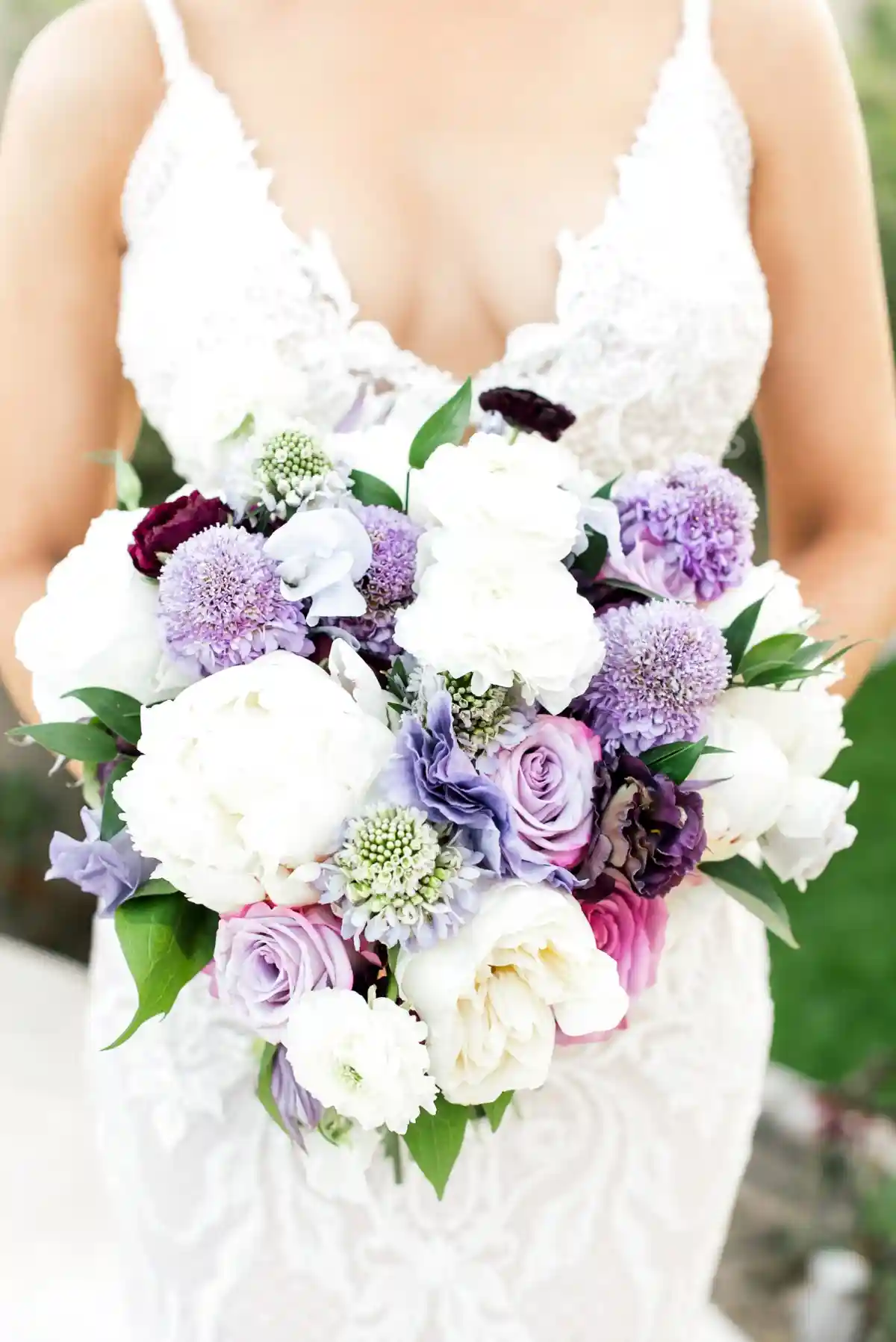 Buquê de noiva com flores lilases, rosas e brancas, em um vestido de noiva detalhado.