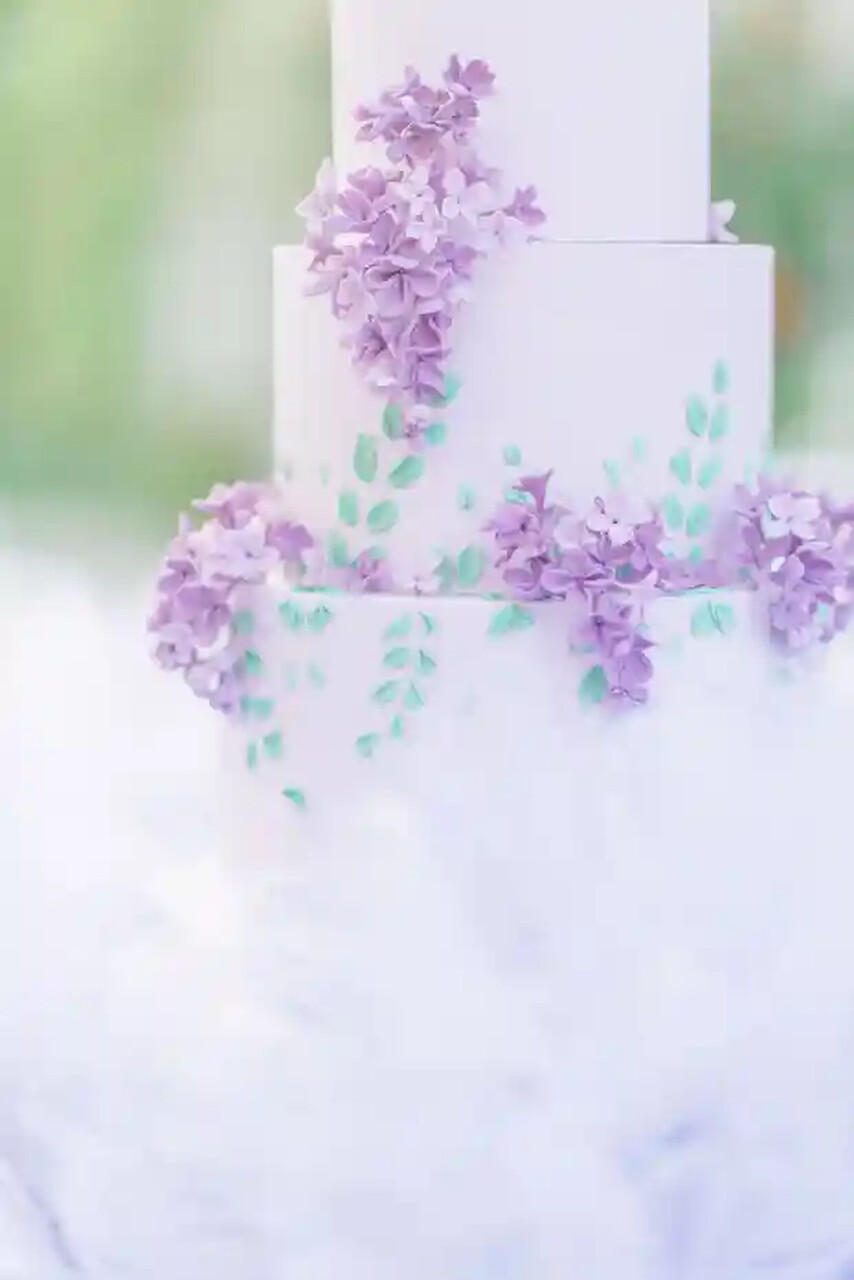 Close-up de um bolo lilás decorado com flores de lavanda em cascata e folhas pintadas