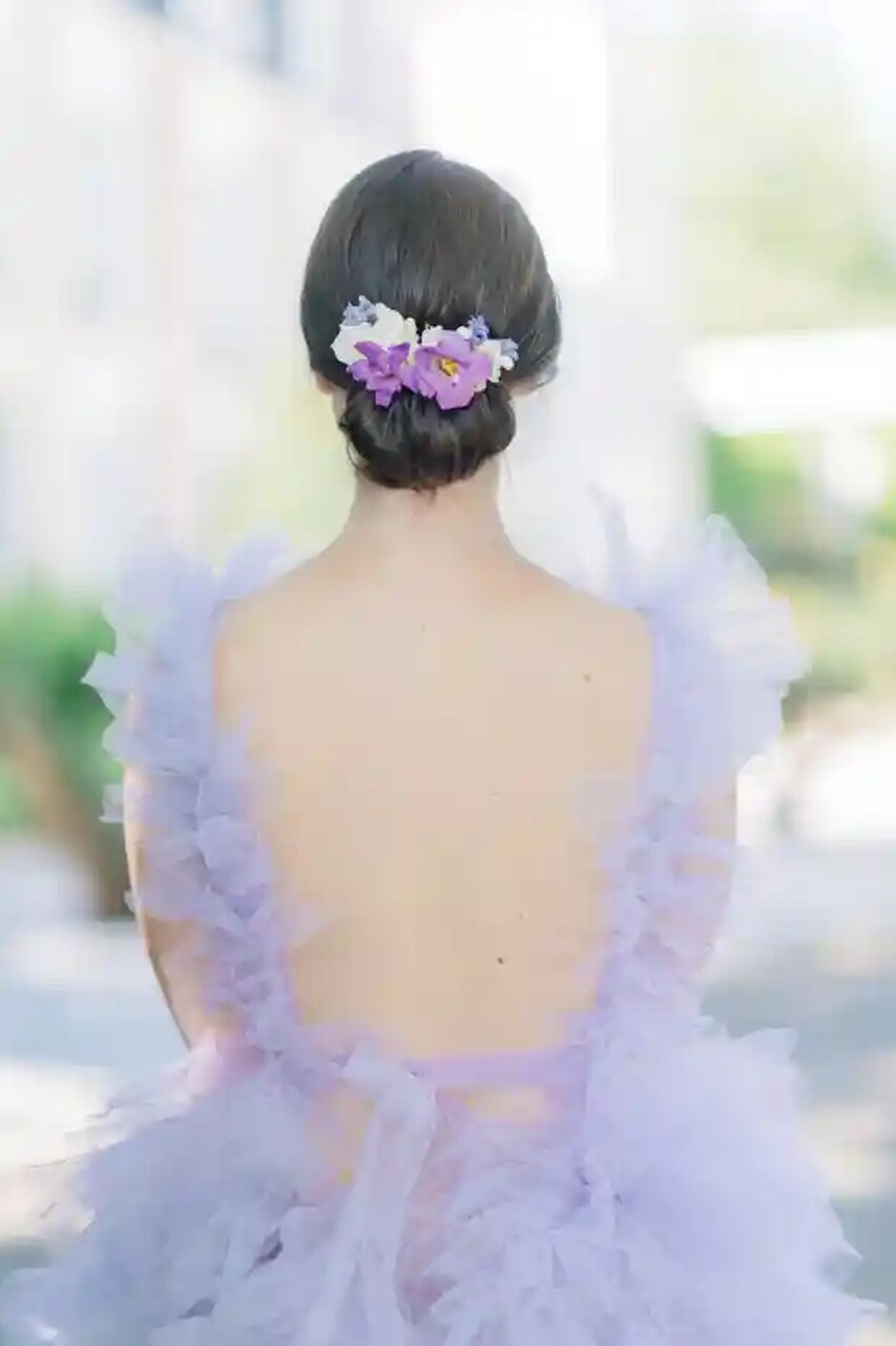 Penteado elegante com coque e flores roxas, em destaque em um vestido com babados lavanda.