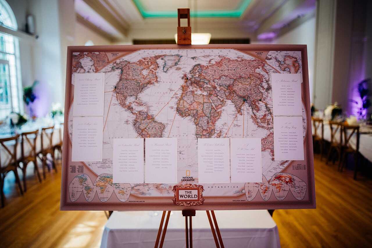 Imagem de um mapa-múndi como painel de assentos em um casamento. A tela exibe os nomes dos convidados com seus respectivos lugares, com uma decoração elegante ao fundo.