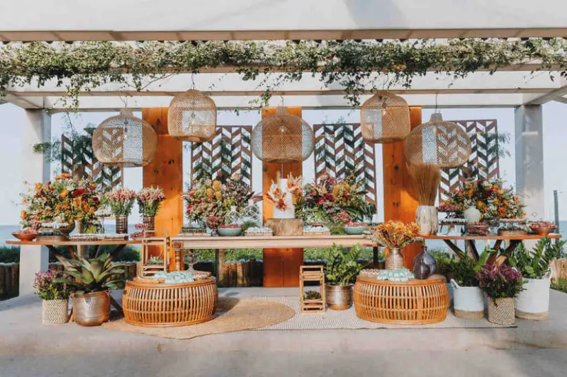 decora&ccedil;&atilde;o apresenta um estilo Boho Chic com fortes elementos r&uacute;sticos e tropicais. &Eacute; uma composi&ccedil;&atilde;o rica em texturas naturais e tons terrosos, ideal para casamentos ao ar livre ou eventos &agrave; beira-mar.