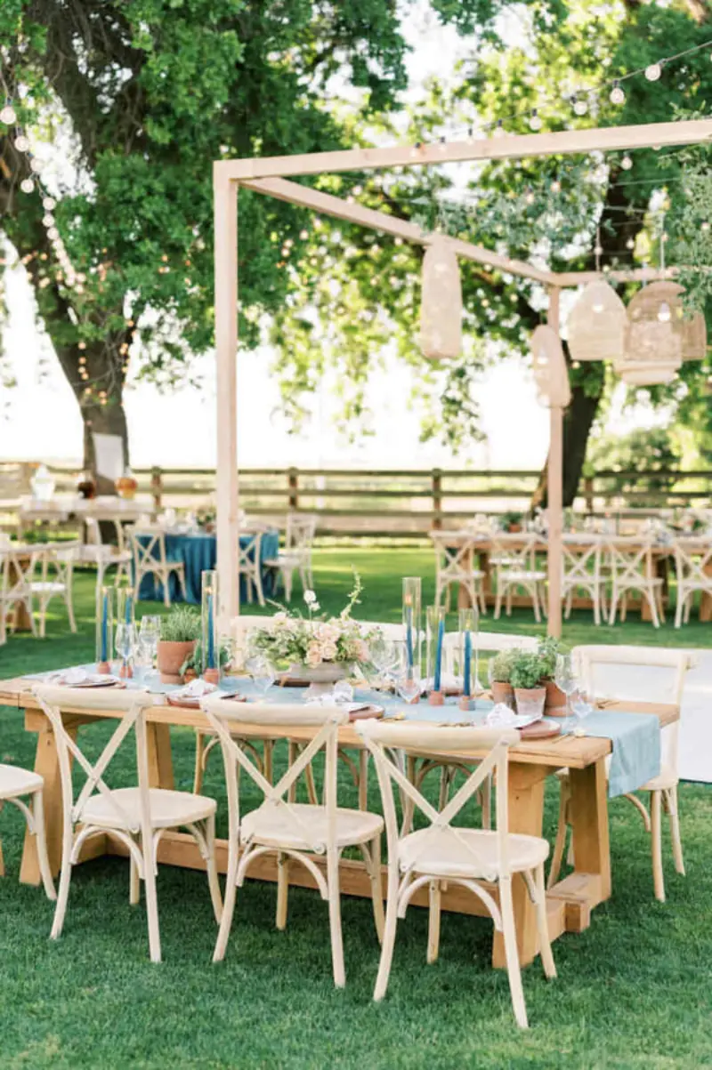 mesa de recep&ccedil;&atilde;o de casamento ao ar livre decorada com elementos r&uacute;sticos e ilumina&ccedil;&atilde;o pendente