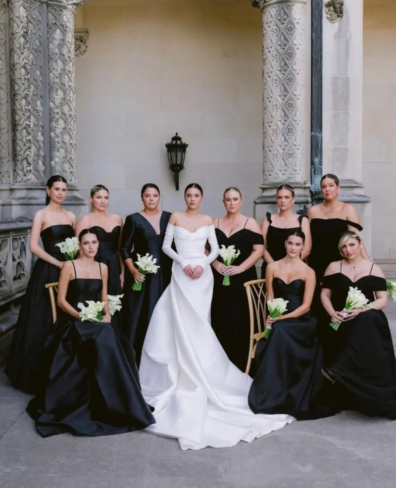 vestido de noiva com decote ombro a ombro e mangas compridas, capturado em um casamento romântico. As madrinhas estão vestindo vestidos pretos