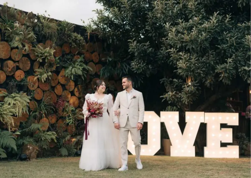 casal em um casamento realizado no campo, com uma decora&ccedil;&atilde;o tem&aacute;tica palavra "LOVE