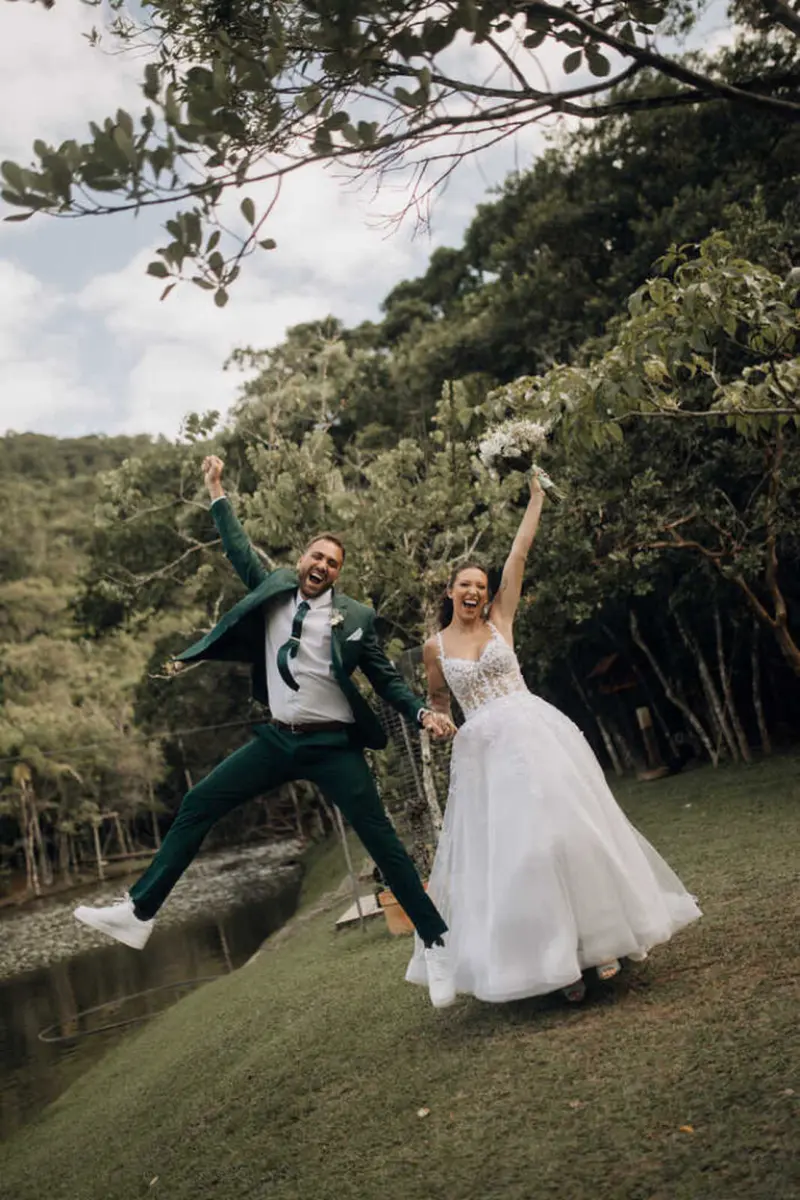 momento espontâneo de alegria do casal saltando em uma área verde arborizada.
