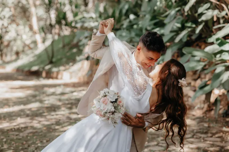Este casal está vestindo trajes tradicionais de casamento, com a noiva usando um vestido de renda branca com mangas longas e o noivo um terno bege