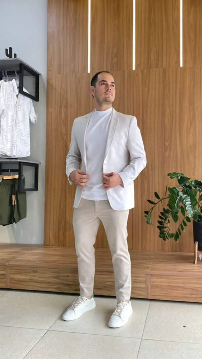 traje esporte fino masculino composto por um blazer bege claro, camiseta branca b&aacute;sica e cal&ccedil;a de sarja ou alfaiataria em tom neutro, finalizado com t&ecirc;nis branco casual