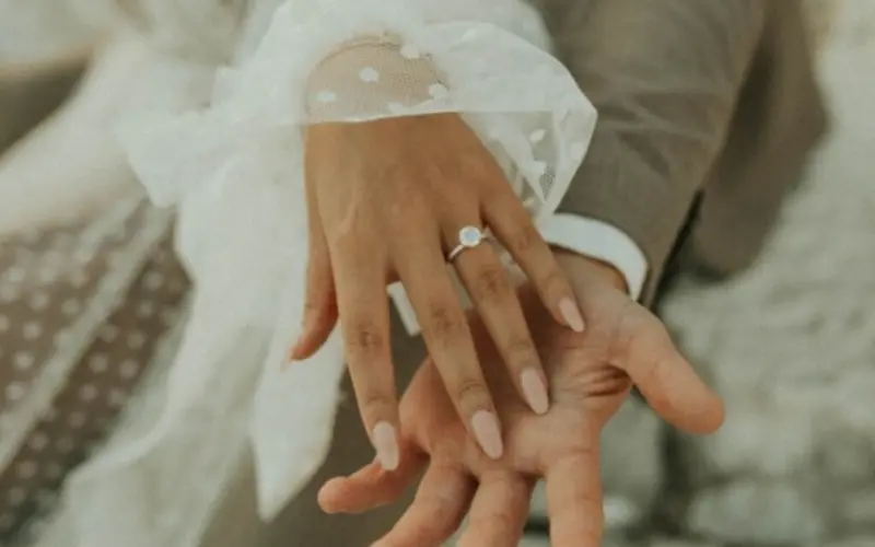 mãos entrelaçadas com um anel de noivado de diamante. A noiva está com a unha no formato estileto