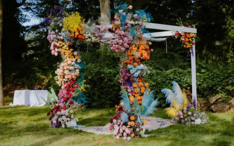 altar de casamento colorido com uma estrutura de madeira com uma instala&ccedil;&atilde;o floral assim&eacute;trica e colorida em tons de azul, laranja, rosa e amarelo
