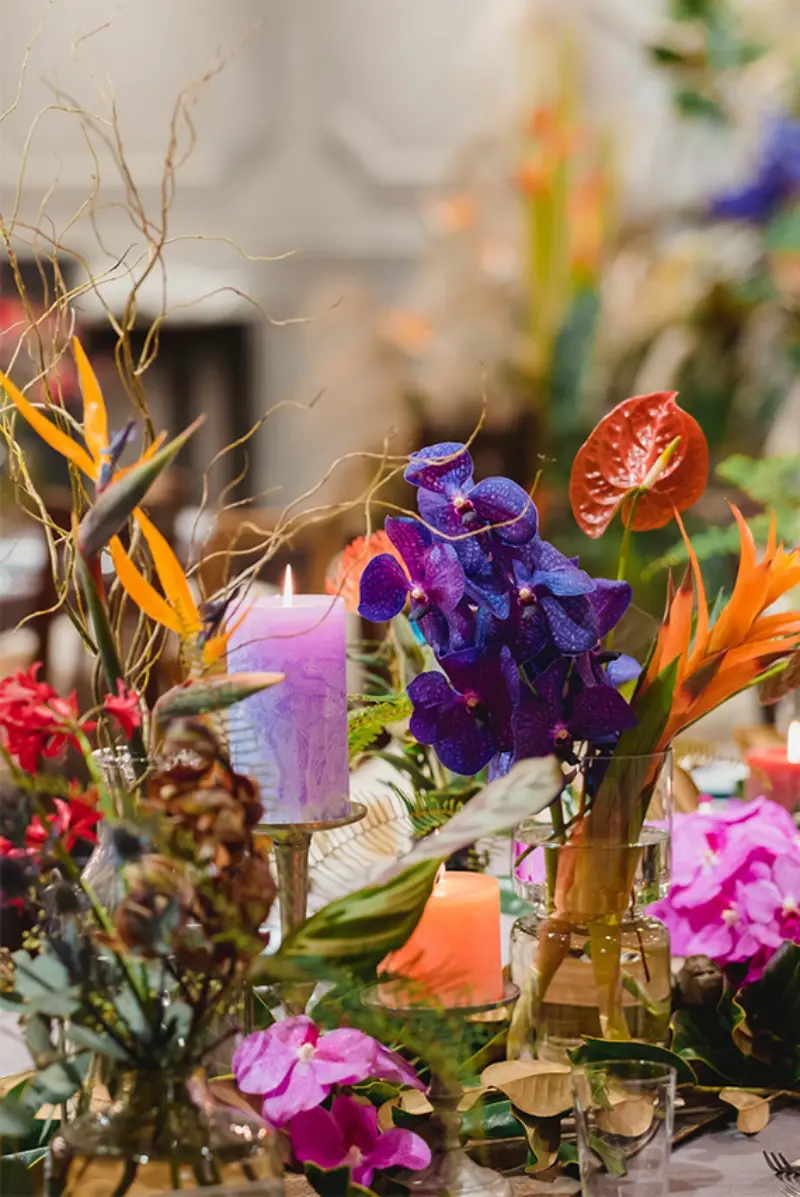 arranjo florais coloridos de mesa de casamento com flores coloridas como ant&uacute;rios vermelhos e orqu&iacute;deas roxas em vasos de vidro