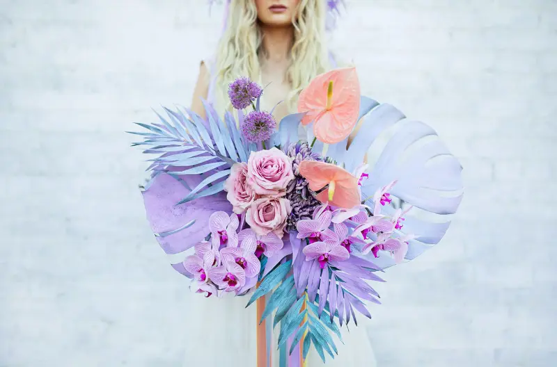 buqu&ecirc; de noiva colorido com flores tropicais e past&eacute;is, incluindo orqu&iacute;deas e rosas, com elementos pintados em tons de lavanda