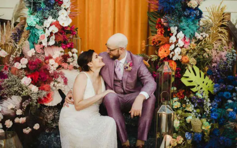 casal posando em frente a uma escada com arranjo floral vibrante com um terno na cor lavanda.