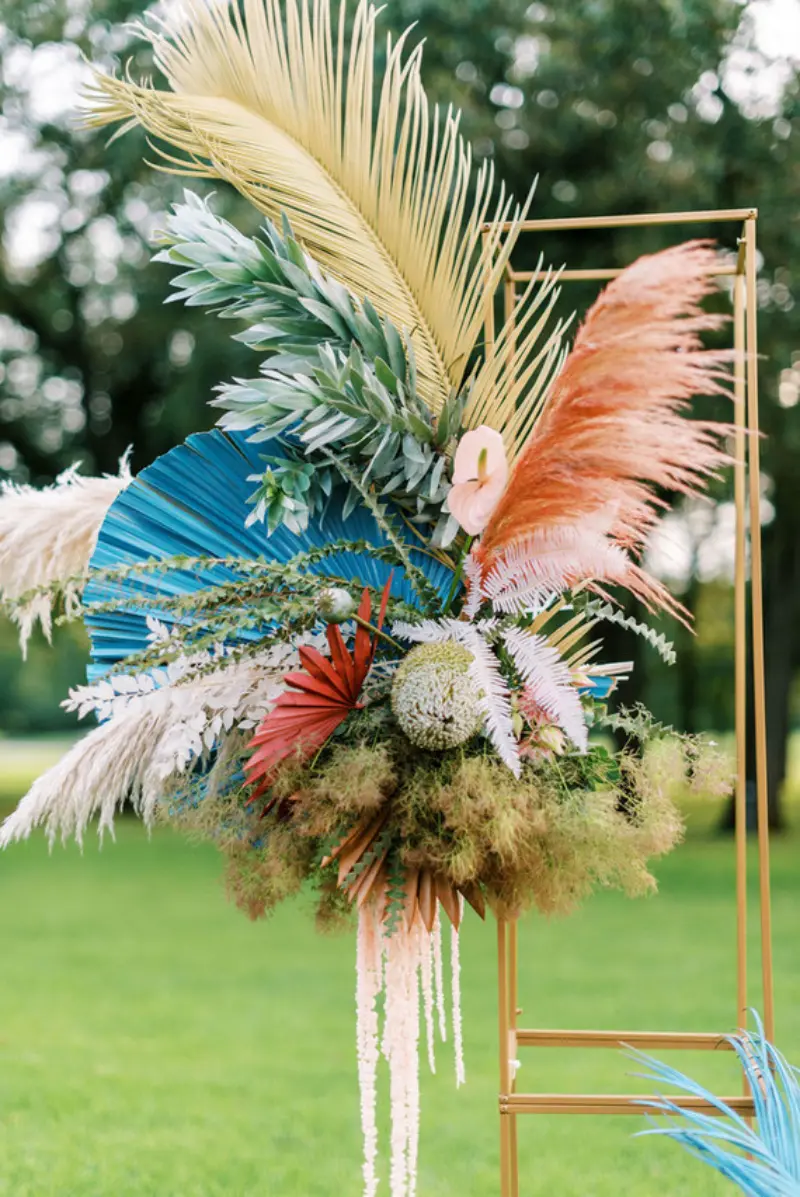 arranjo de casamento colorido apresenta uma mistura vibrante de elementos desidratados e tropicais, incluindo capim-dos-pampas tingido de azul e rosa