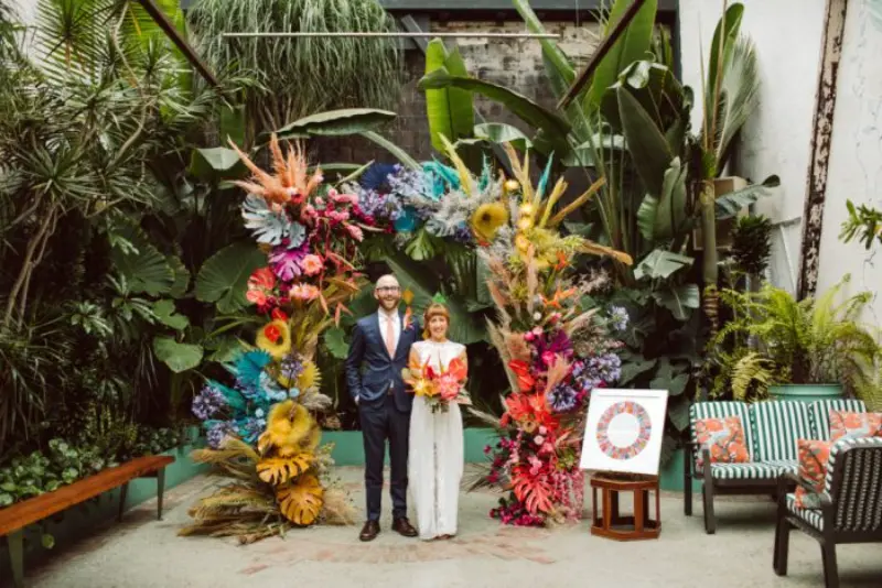 decora&ccedil;&atilde;o de casamento colorido e casal sob um arco floral colorido.