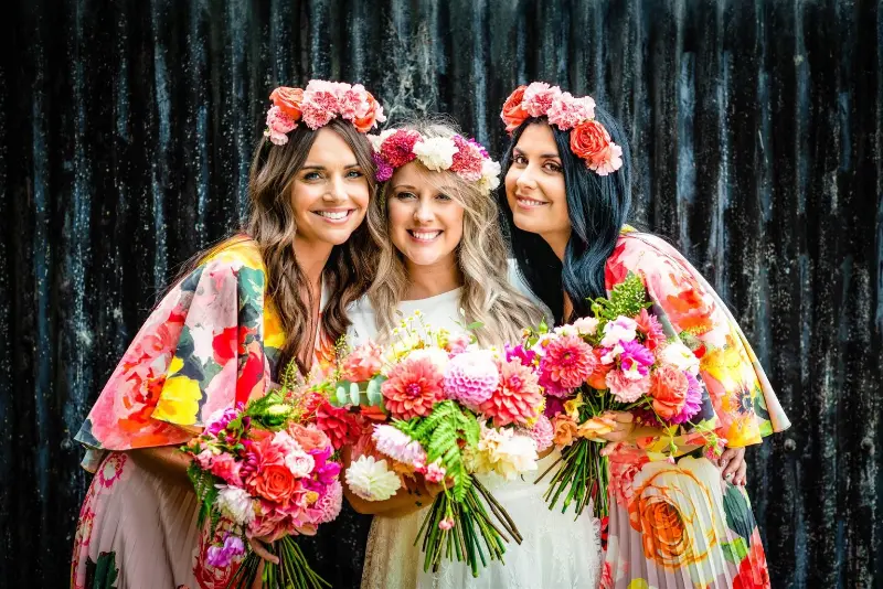 tr&ecirc;s madrinhas vestindo quimonos coloridos com estampas florais e coroas de flores combinando