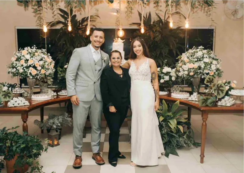 Adriana Vitti ao lado dos noivos em frente da mesa de doces