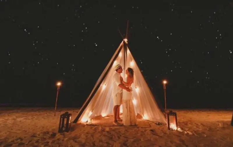 casal em cabana na praia com luzes criando um clima rom&acirc;ntico