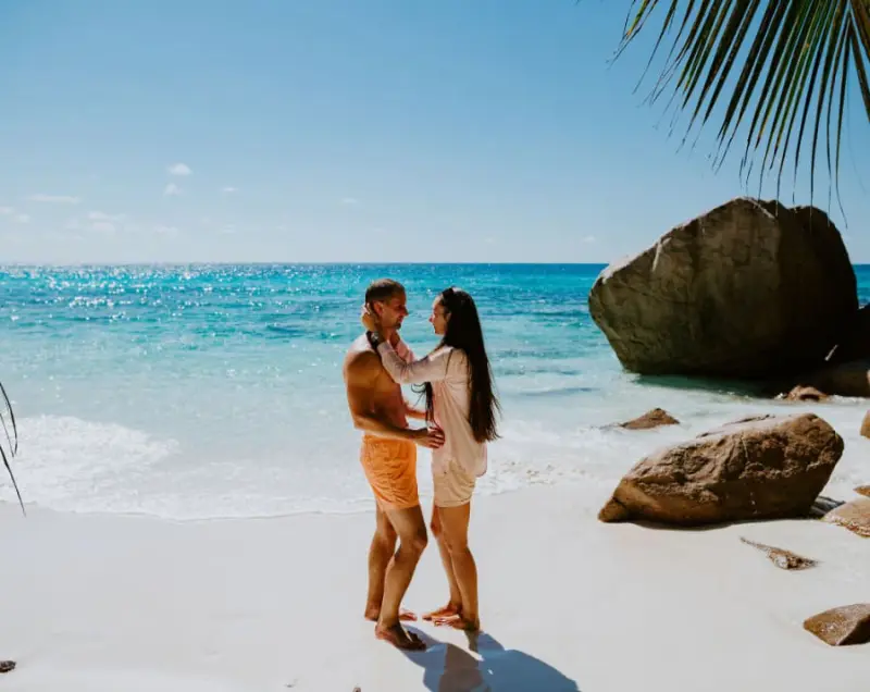 casal na praia em viagem feita por ag&ecirc;ncia para lua de mel