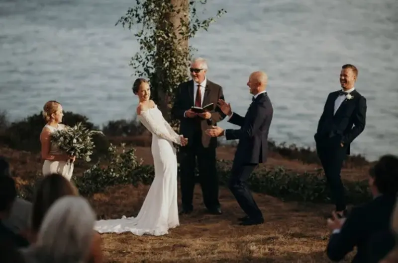 celebrante de casamento fazendo noivos rirem em cerim&ocirc;nia com vista para o mar