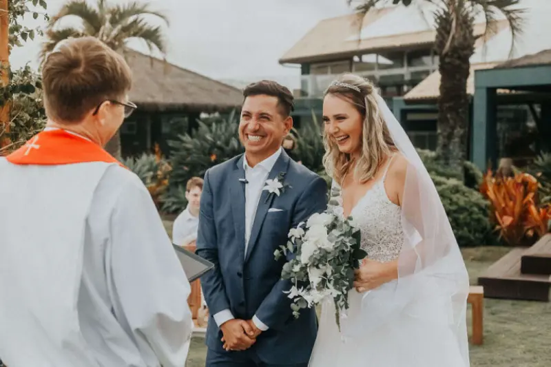 noivos rindo durante a cerim&ocirc;nia de casamento ao ar livre