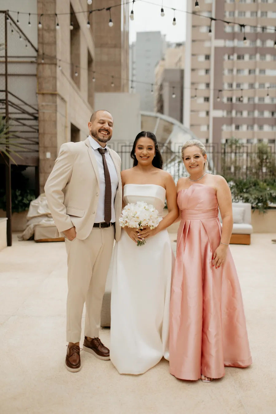 noiva ao lado do pai de terno bege e mãe de vestido rosa