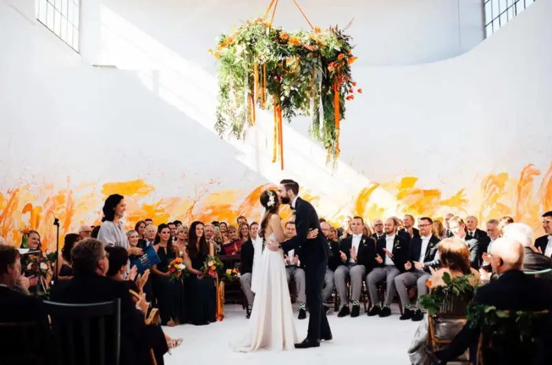 noivos est&atilde;o ao centro e convidados ao redor observando o beijo. A decora&ccedil;&atilde;o de casamento amarelo