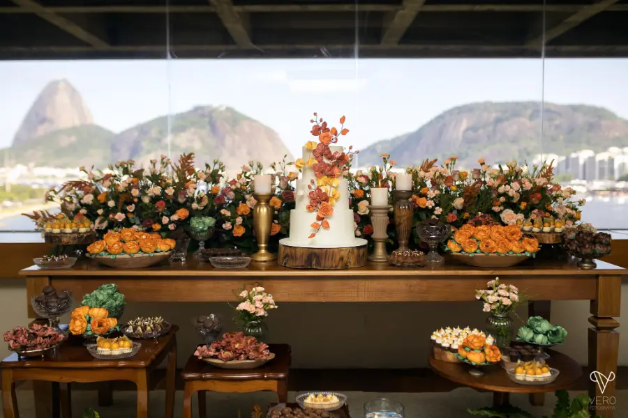 mesa do bolo decorada com flores de cores quentes