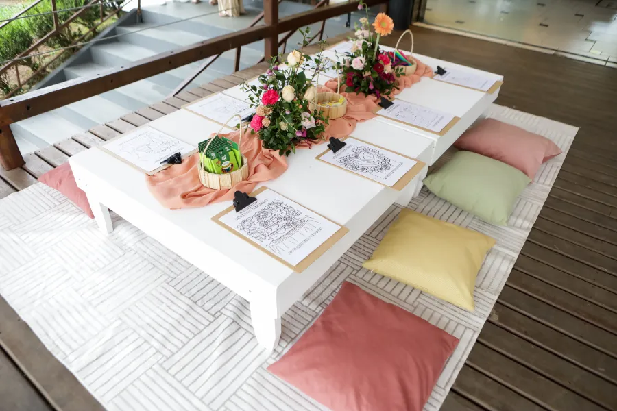 Espaço de relaxamento infantil em casamento com mesa baixa, almofadas coloridas e arranjos florais