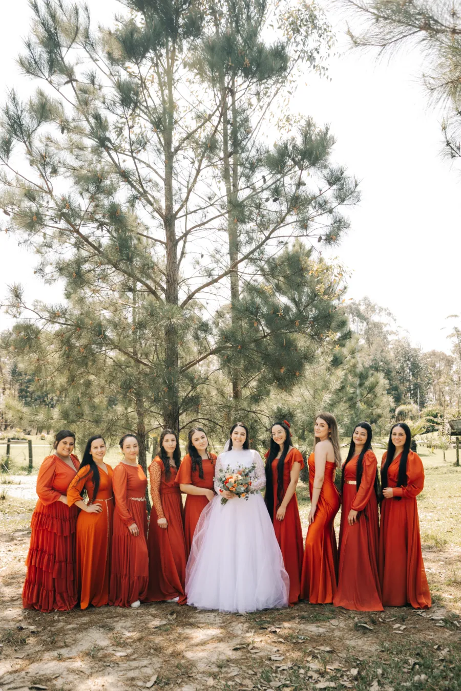 A noiva posa com suas madrinhas, todas usando vestidos cor terracota, em um cenário natural, típico de um casamento terracota ao ar livre.