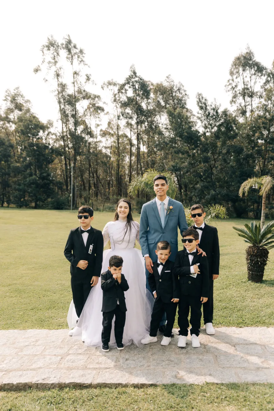 Foto de grupo dos noivos com pajens em trajes formais, em um jardim