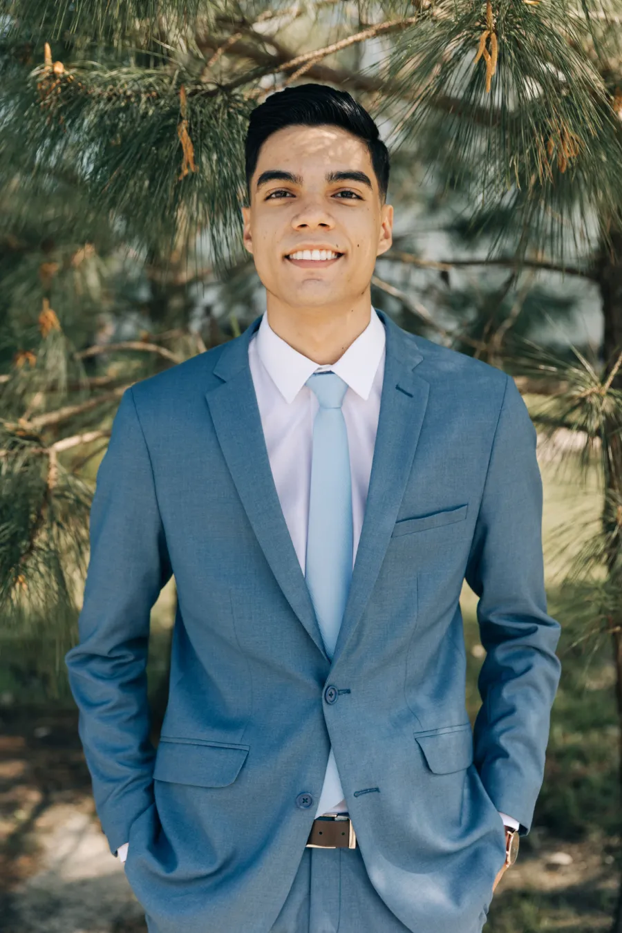 Retrato do noivo sorrindo, vestindo um terno azul, em meio à vegetação