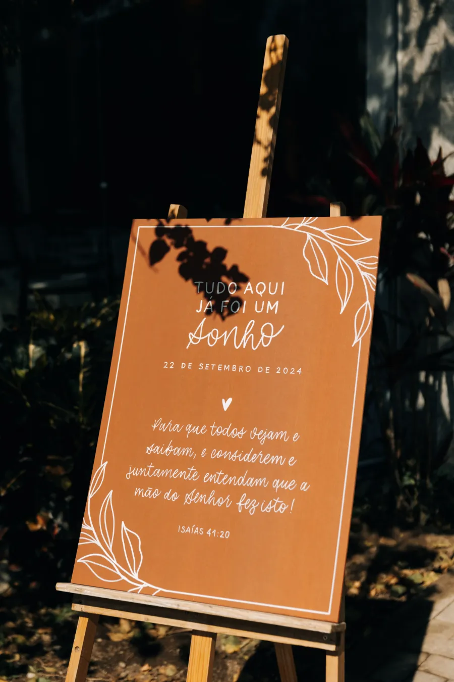  Um quadro de boas-vindas em tom terracota com texto em português e decoração floral branca, indicando o tema do casamento terracota.