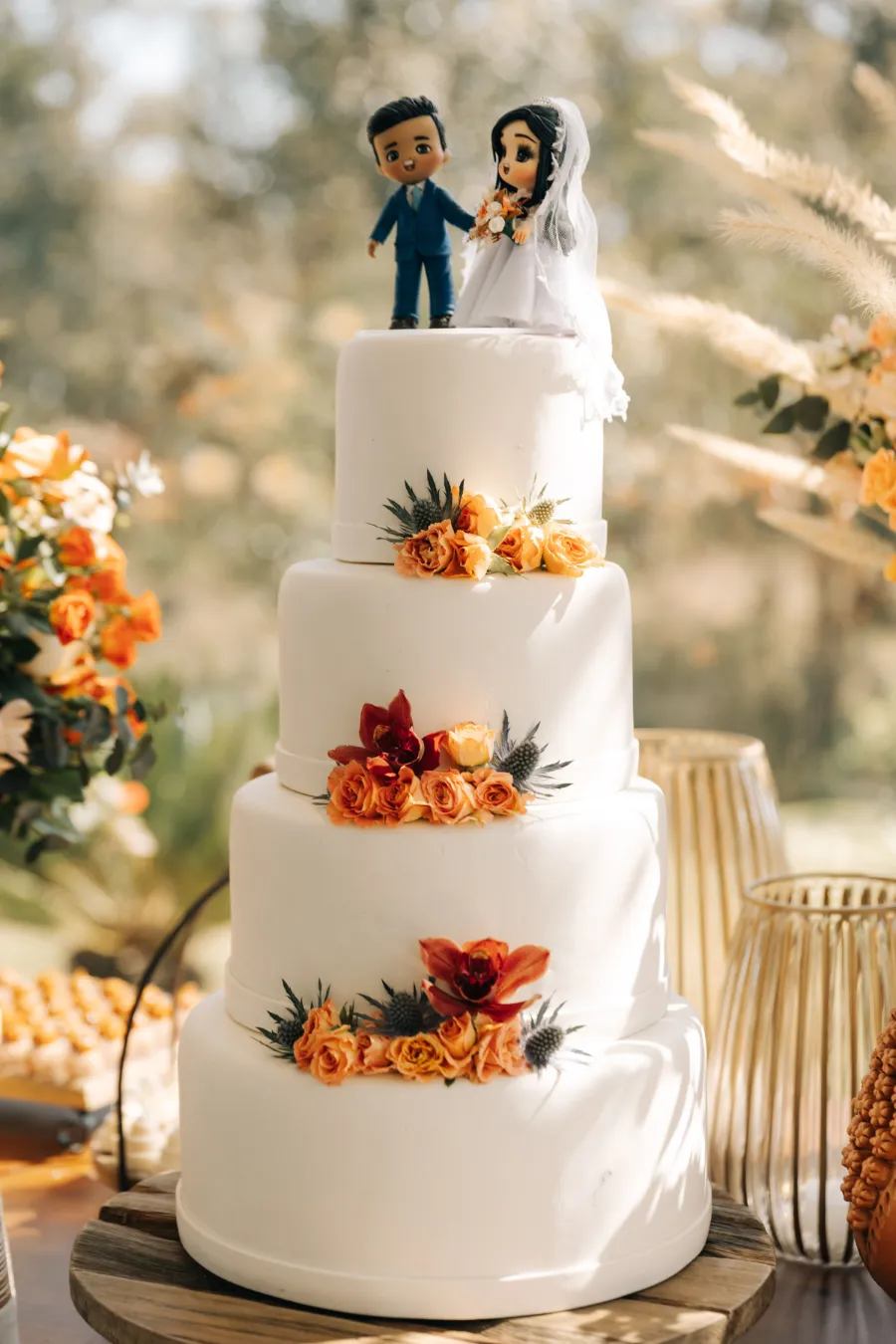 Bolo de casamento de vários andares decorado com flores em tons de laranja e terracota e um topo de bolo personalizado, destacando o tema do casamento terracota.