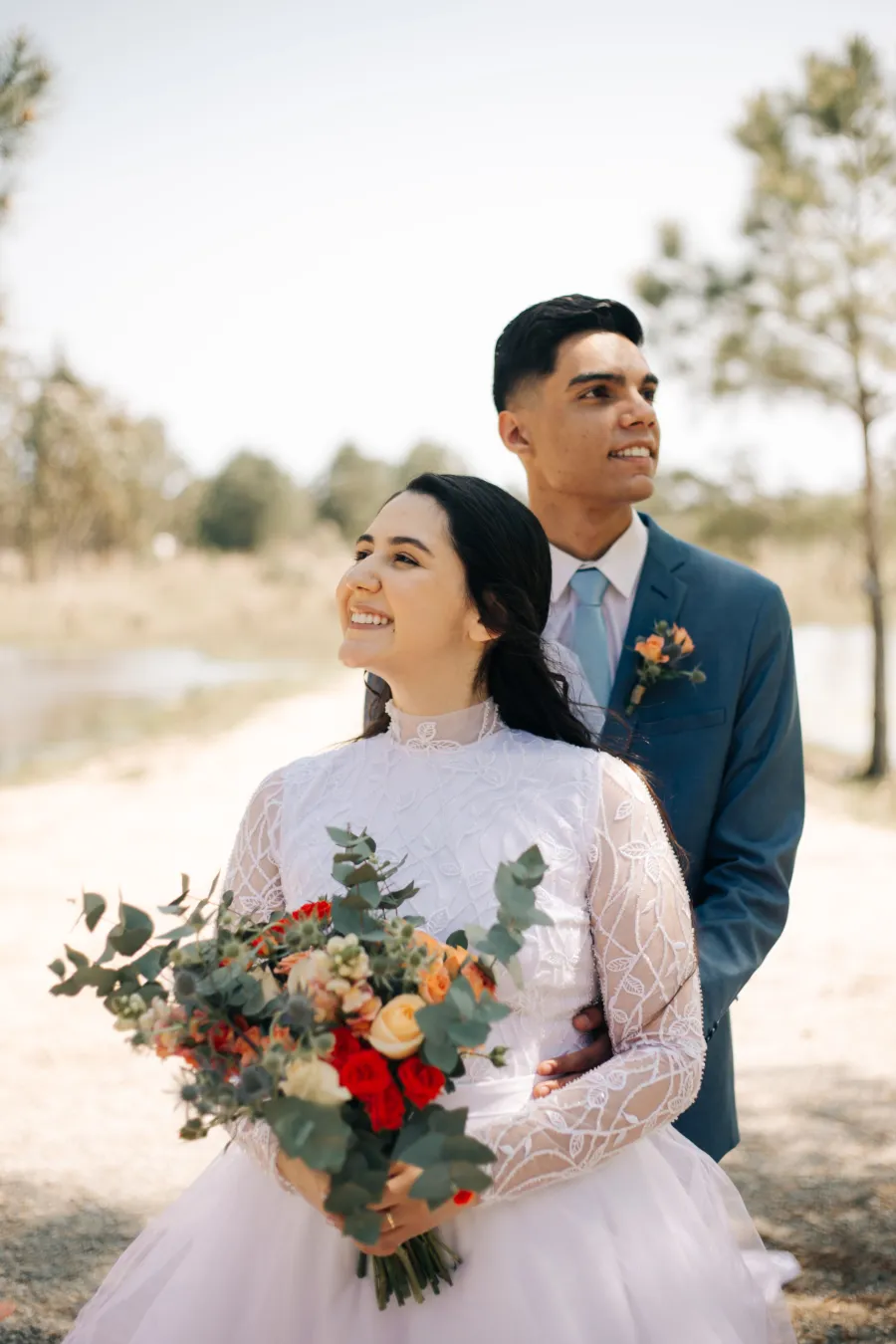 Retrato dos noivos ao ar livre, a noiva segurando um buquê com flores em tons de terracota e folhagens