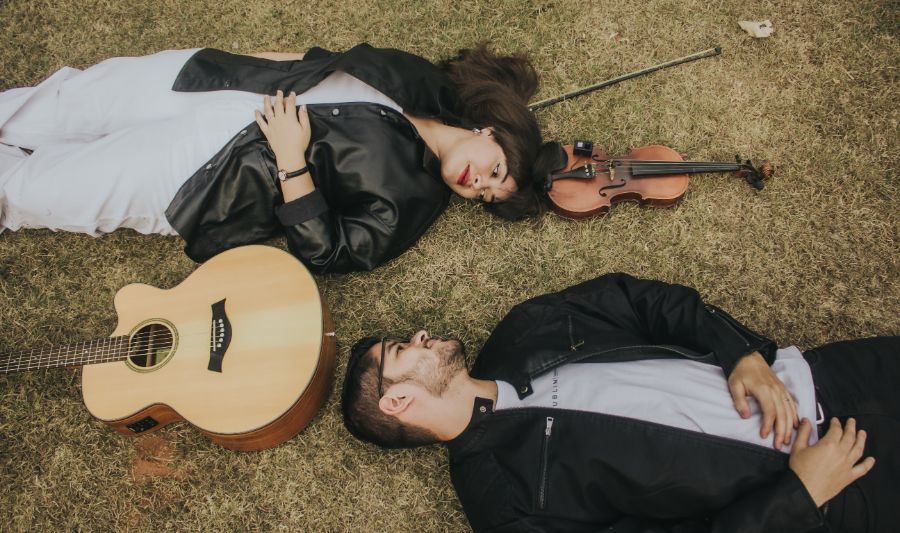 noivos deitados na grama ao lado de instrumentos musicais