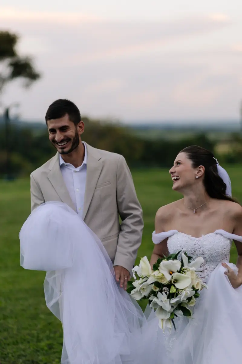 noivos caminhando no campo com noivo segurando venstido da noiva