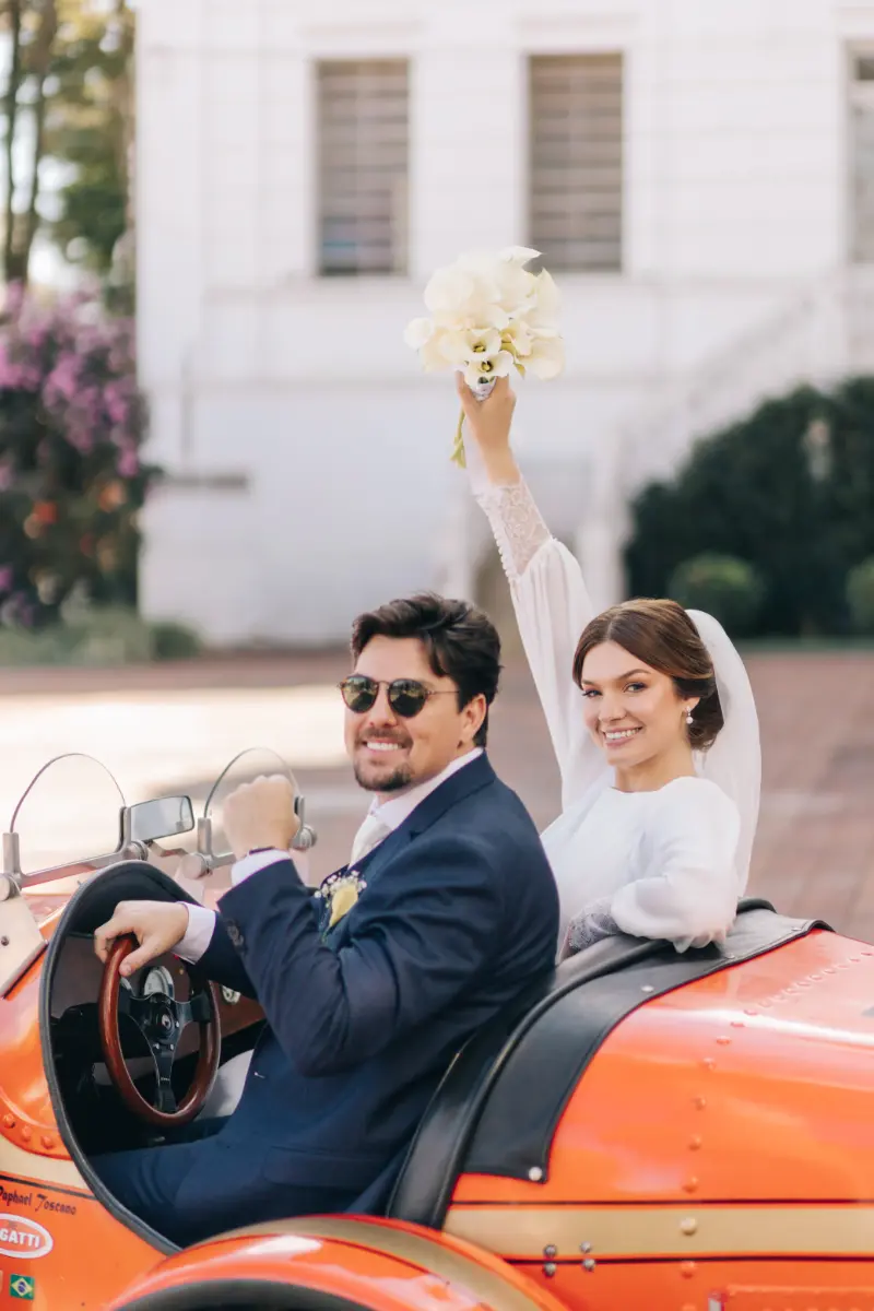 saída dos noivos em carro antigo sorrindo para foto do Gustavo Quagliato Fotografia