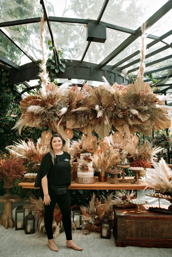 capa post: La Belle Assessoria em frente a mesa de bolo com arranjos suspensos