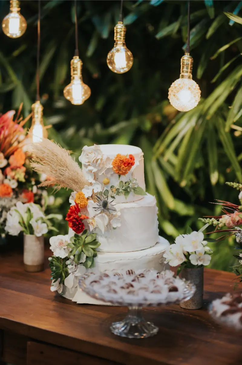 bolo de casamento com lâmpadas suspensas em mesa de doces