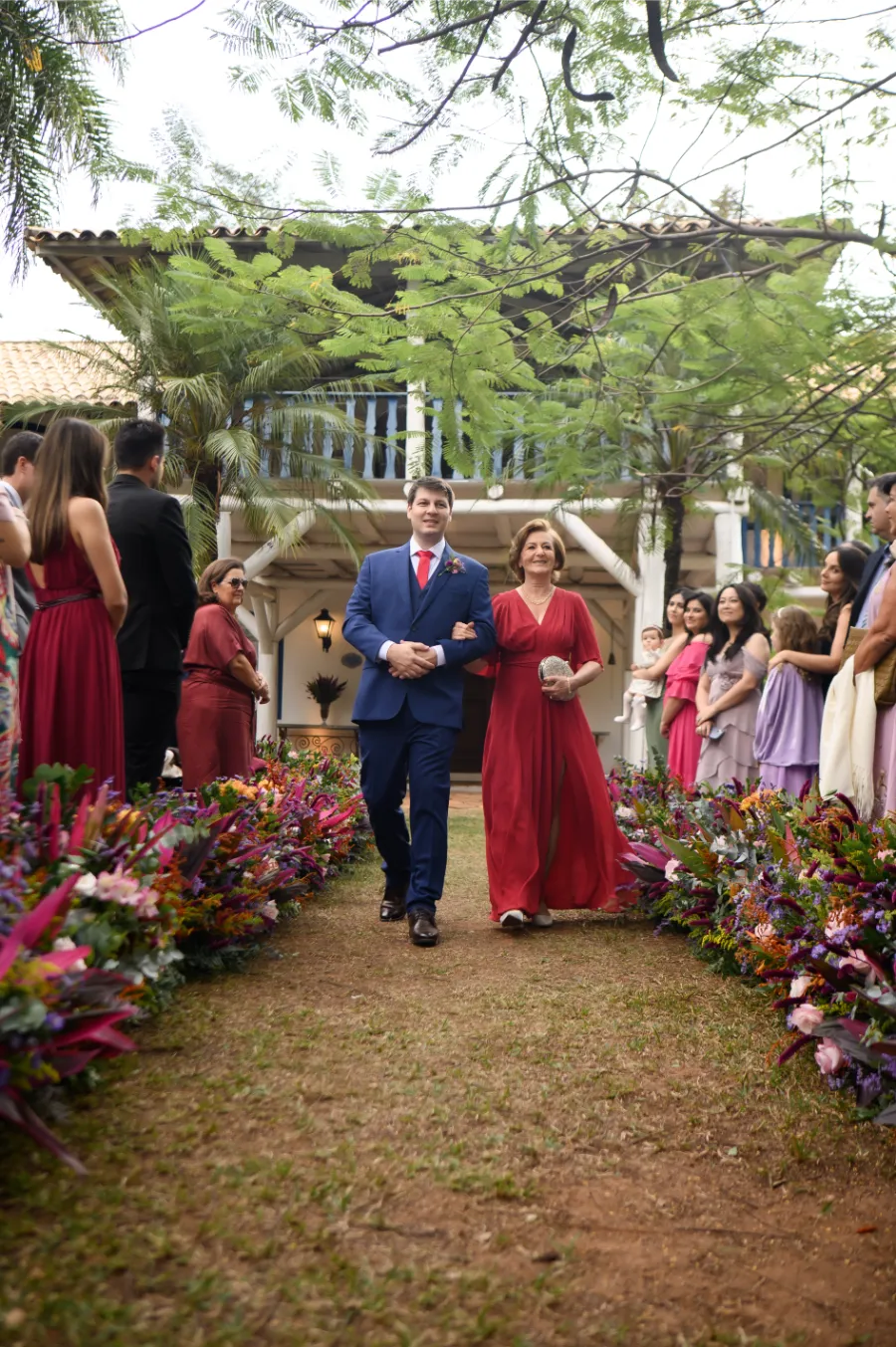 entrada do noivo com terno azul e mãe com vestido vermelho