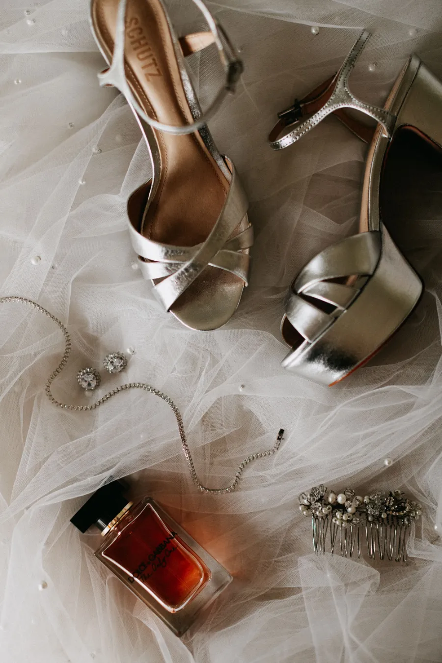 sandália prateada ao lado de perfume e colar