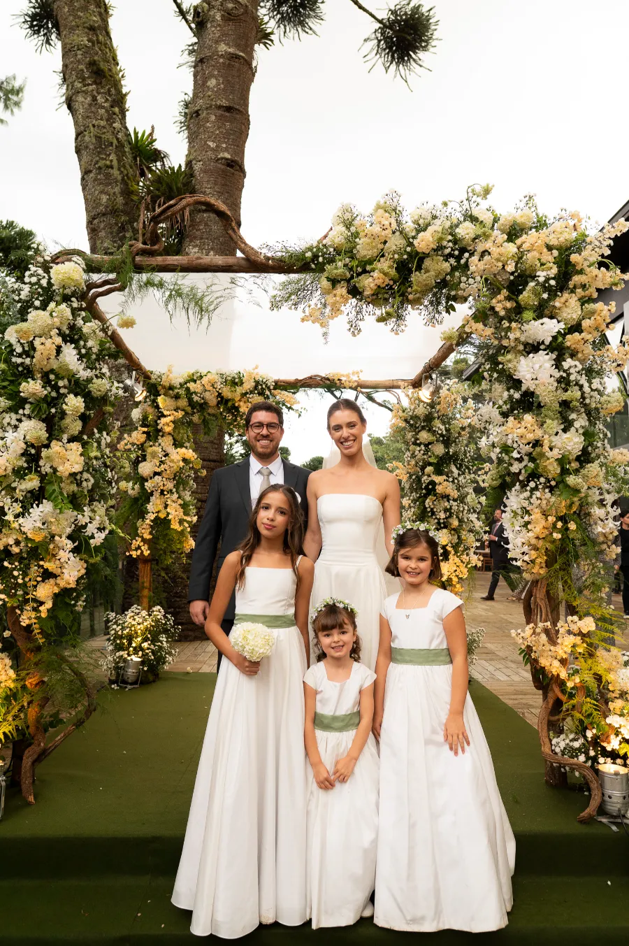 daminhas com vestido com faixa verde e noivos atrás