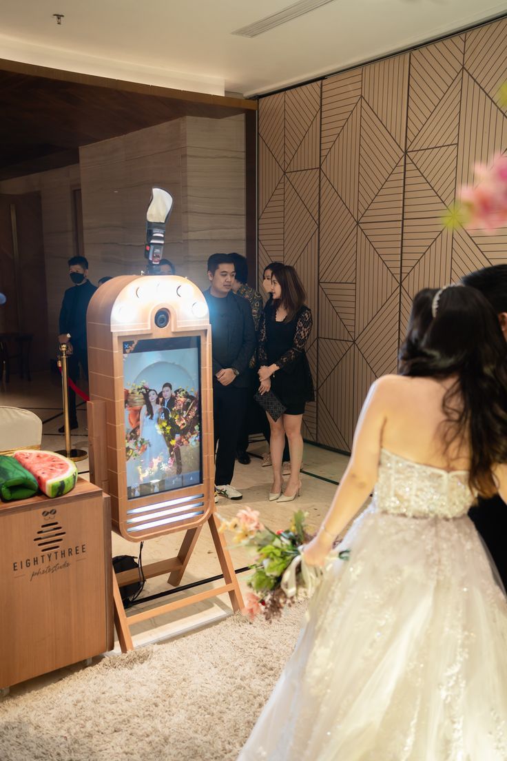 Totem de fotos em casamento exibindo imagem dos noivos na tela, com convidados aguardando na fila.