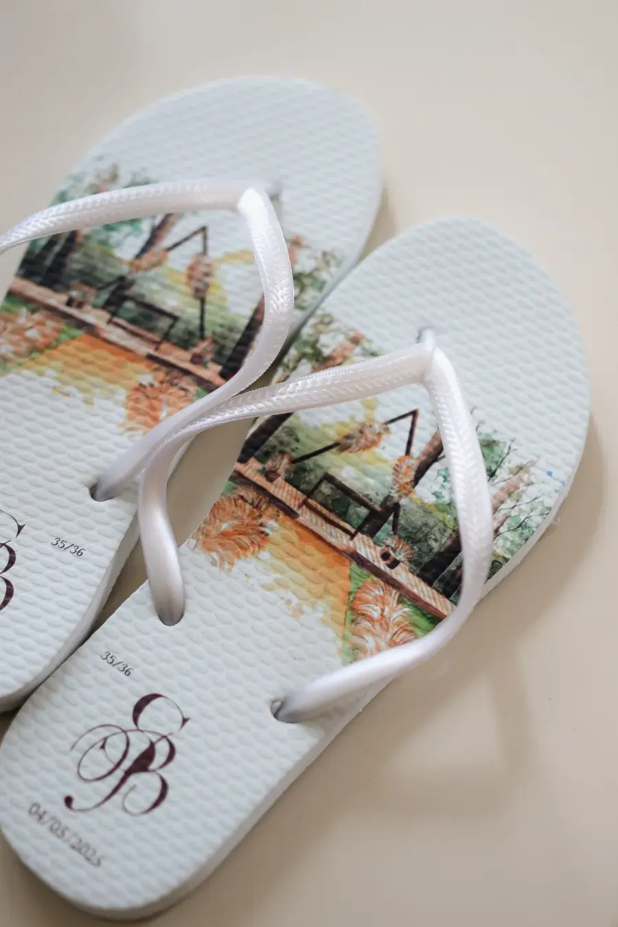 Chinelos personalizados brancos com tiras acetinadas e estampa aquarela de paisagem, iniciais B e G e data do casamento.